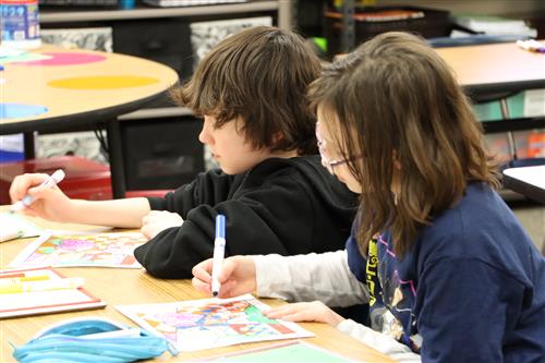 Two students coloring a math sheet at a table.